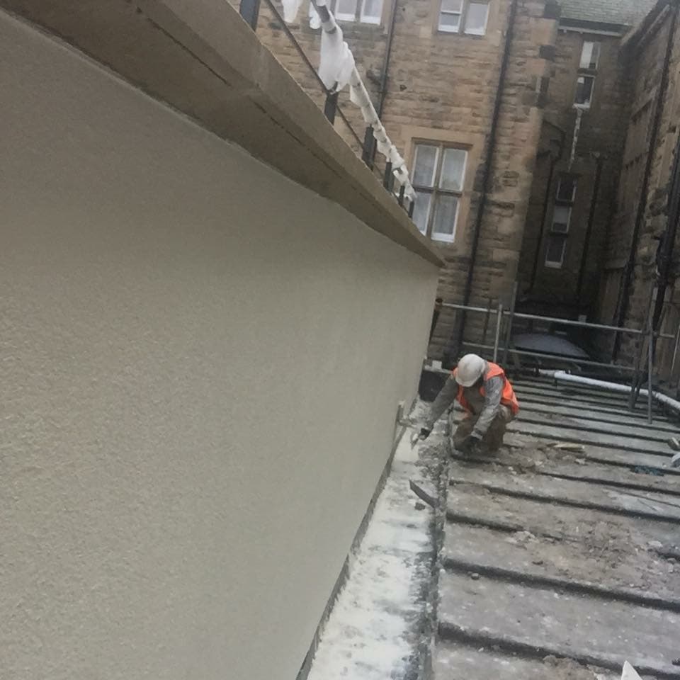 Construction worker in safety gear finishing the base of a freshly plastered exterior wall.