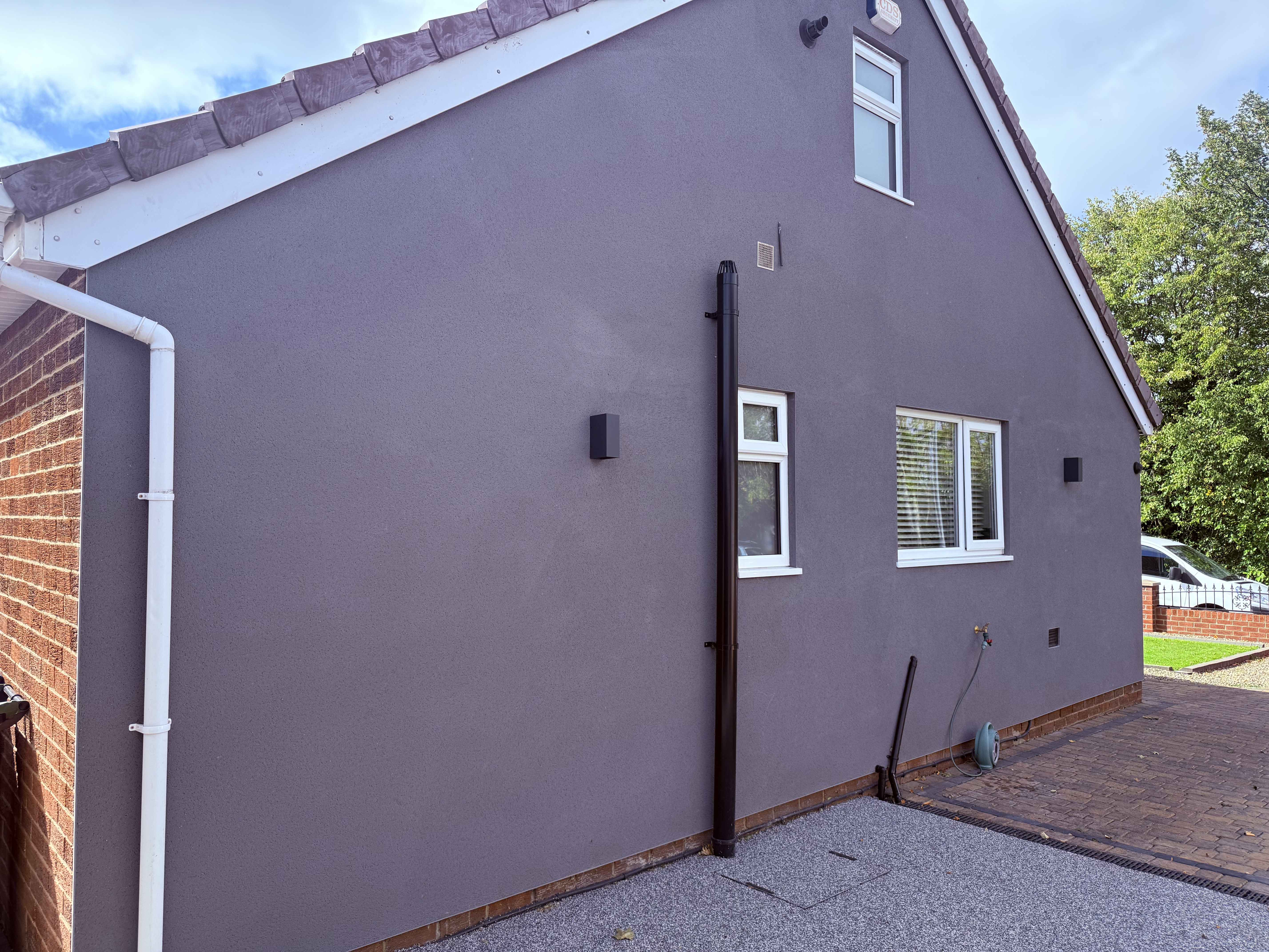 Side view of a modern house with grey textured render, white windows, and black pipework.