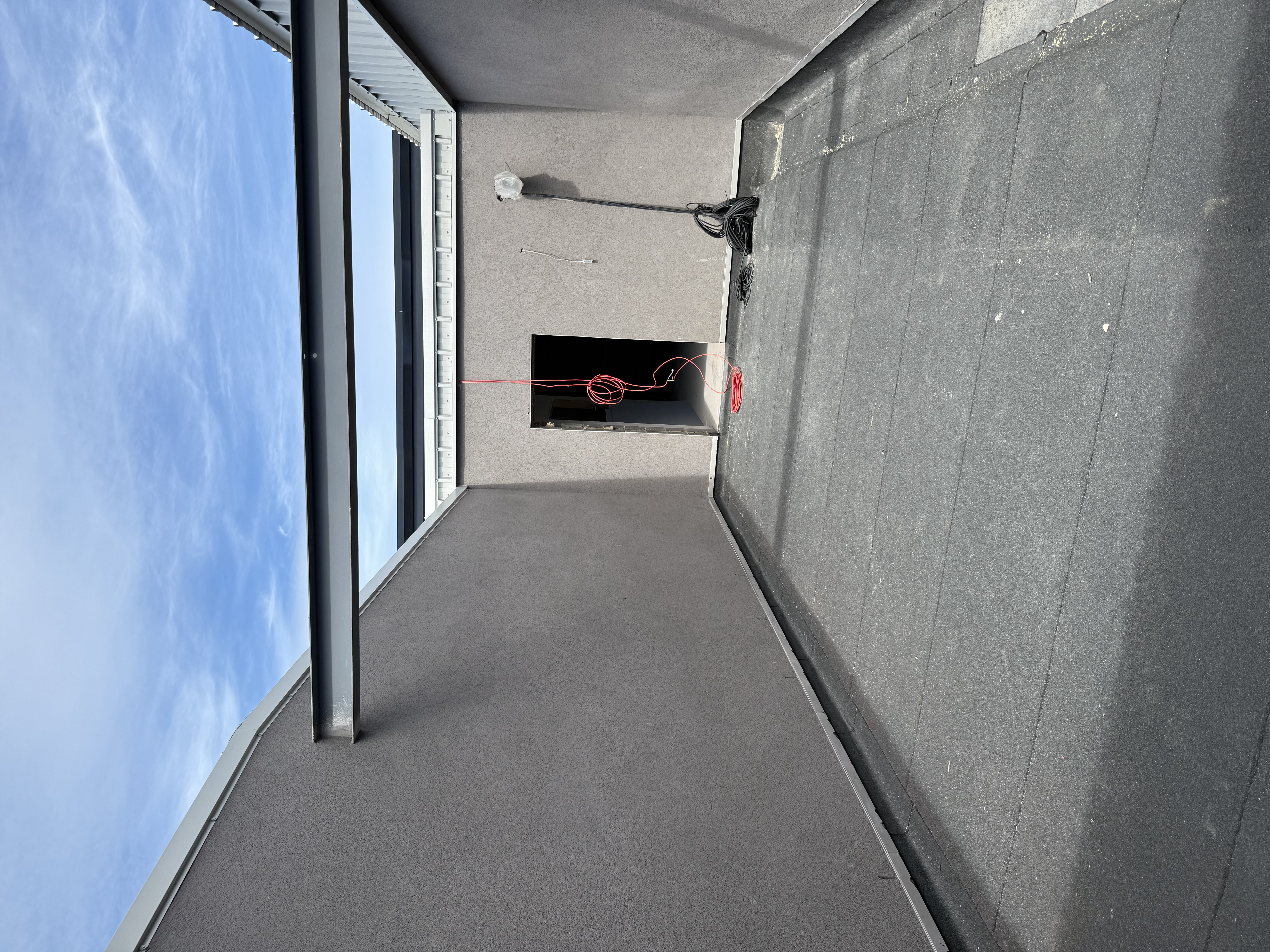 Rooftop construction area with grey walls, dark flooring, and hanging red electrical cables.